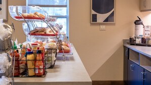 A breakfast bar with a variety of food items and condiments, a coffee machine, and a window with natural light. - TownePlace Suites by Marriott Gahanna (Columbus)