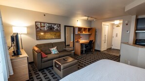 A hotel room with a bed, a sofa, a desk, a lamp, and a painting on the wall. - TownePlace Suites by Marriott Gahanna (Columbus)