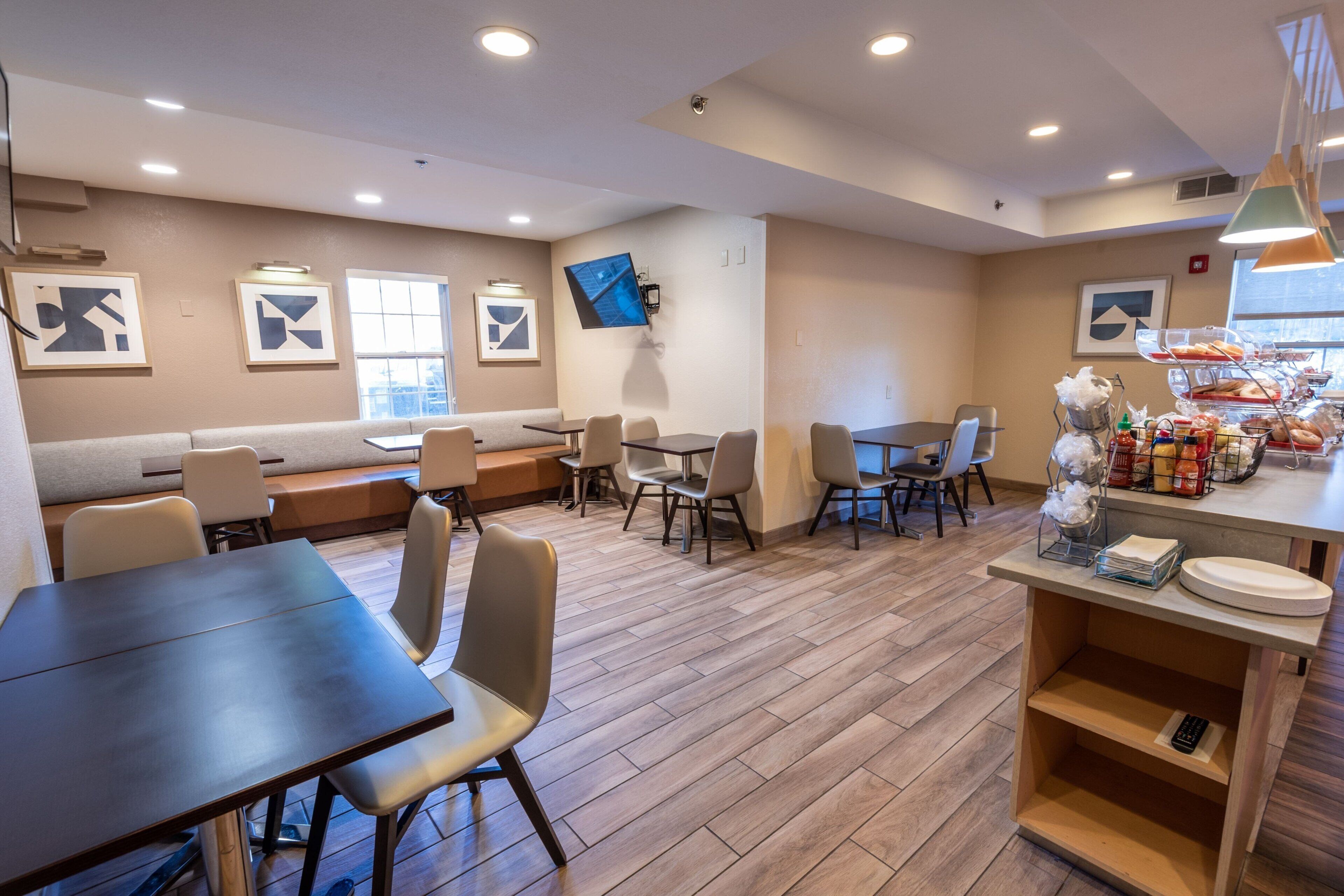 A modern dining area with a long table, several chairs, a bench, and a buffet counter with food items.