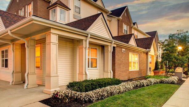 A row of townhouses with a covered front porch, brick exterior, and a landscaped front yard. - TownePlace Suites by Marriott Gahanna (Columbus)