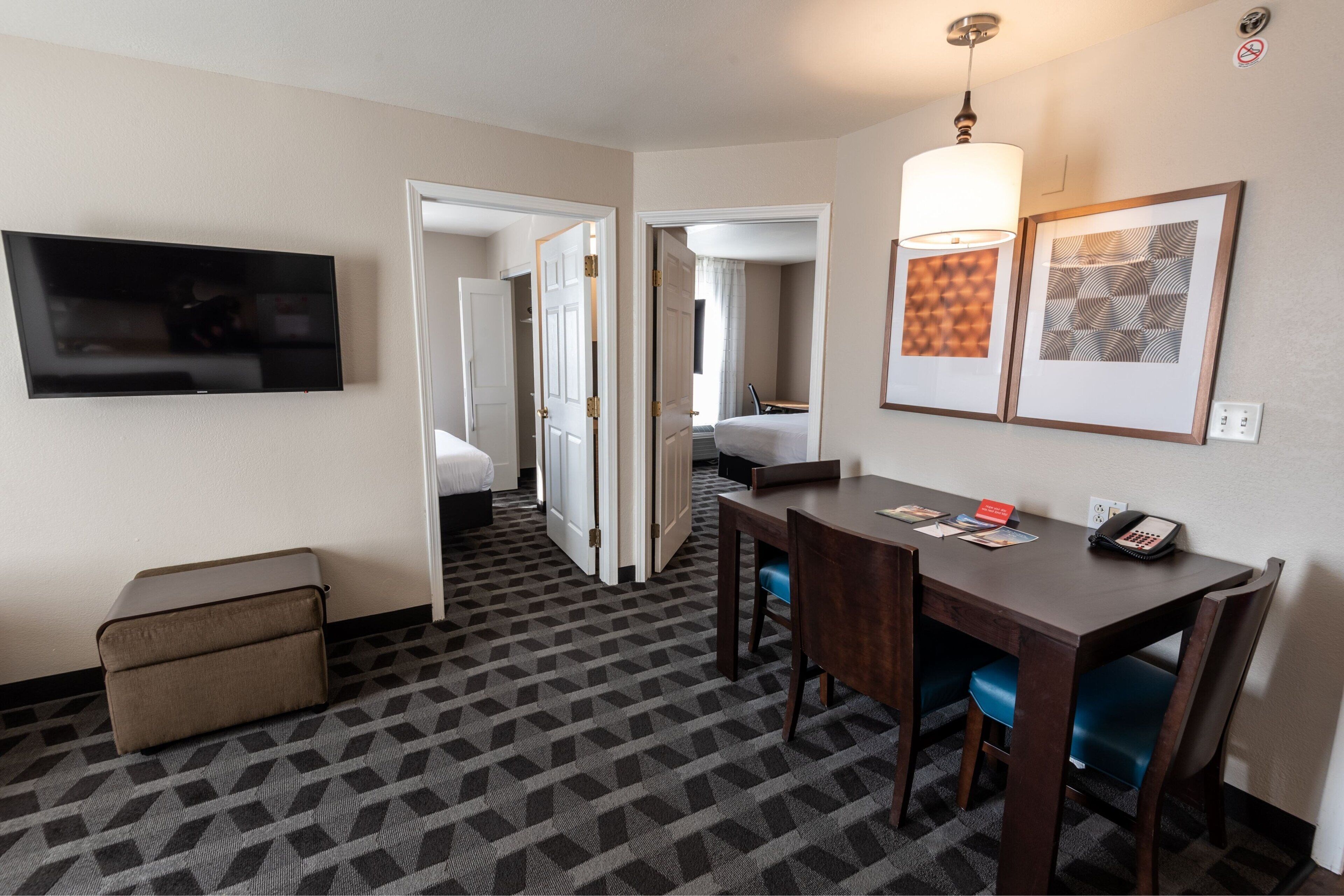 Ein Hotelzimmer mit Fernseher, einem Esstisch mit Stühlen, einem Bett und einem durch eine offene Tür einsehbaren Badezimmer.