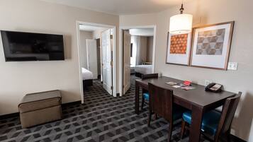 Ein Hotelzimmer mit Fernseher, einem Esstisch mit Stühlen, einem Bett und einem durch eine offene Tür einsehbaren Badezimmer.