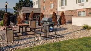 Un patio con una parrilla, una mesa de picnic y mobiliario exterior.