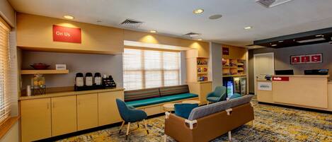 A hotel lobby with a reception desk, seating area, and a kitchenette.