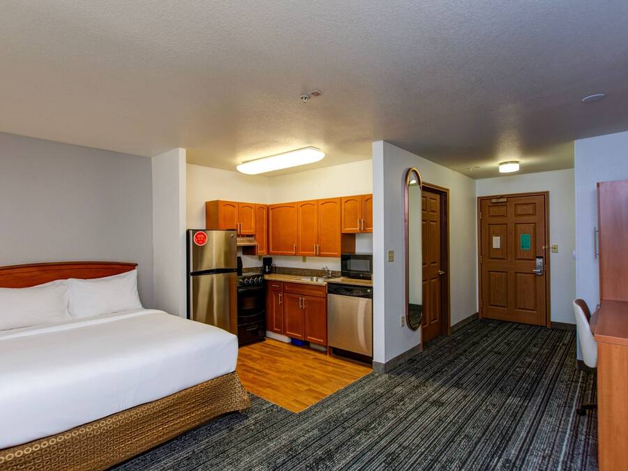 Habitación de hotel compacta con cama, kitchenette y pequeña zona de escritorio.