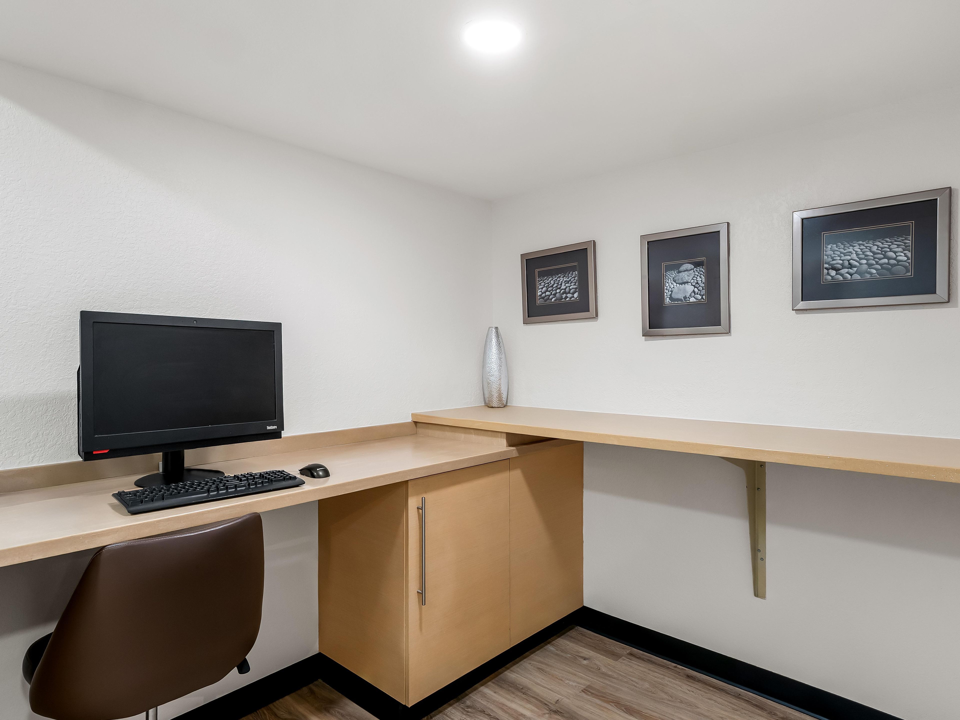 A workspace with a desk, computer monitor, keyboard, and chair. There are three framed pictures on the wall.
