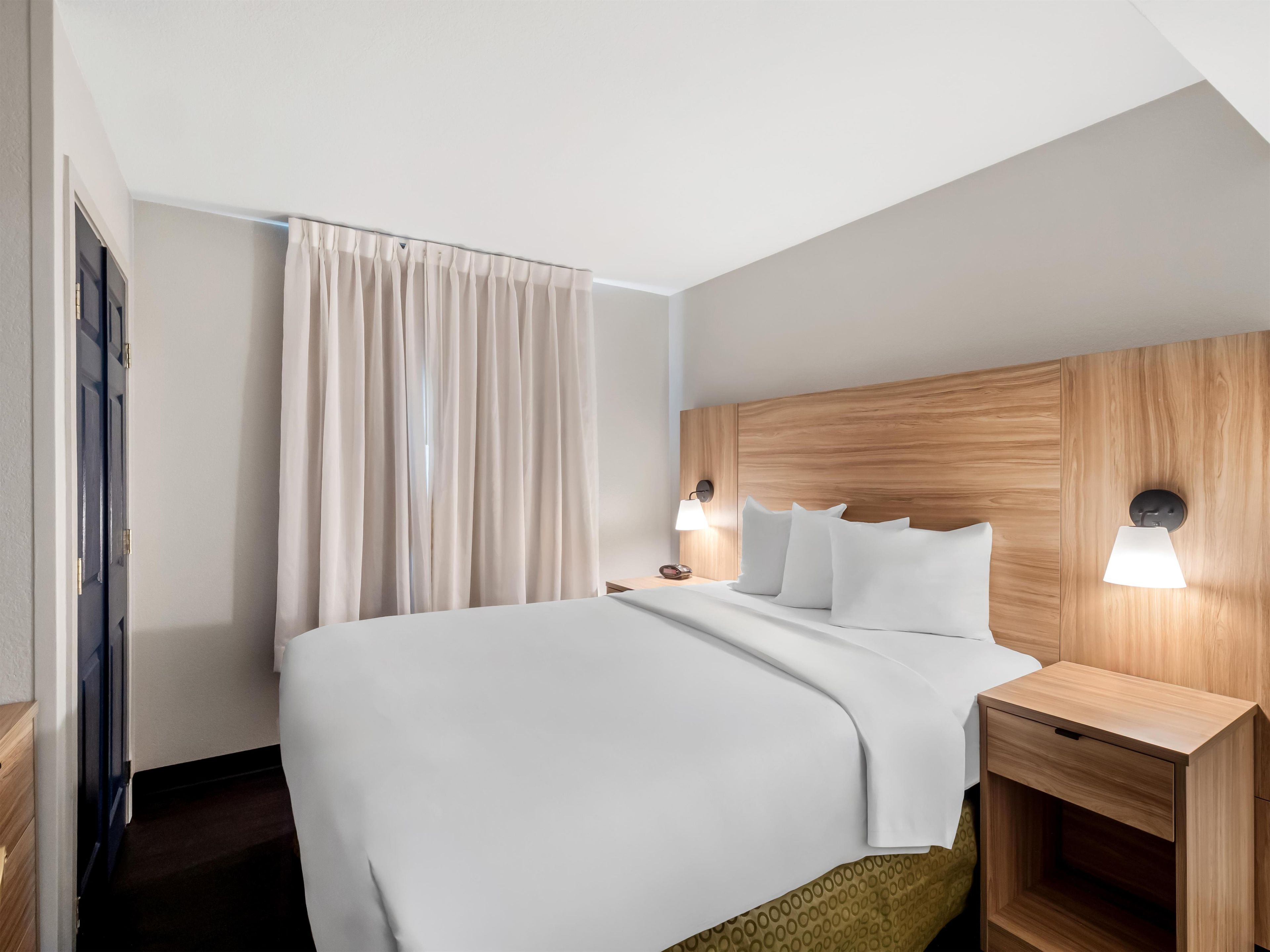 A hotel room with a bed, bedside tables, and a wooden headboard.