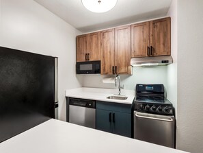 A compact kitchen with a dishwasher, microwave, stove, and wooden cabinets. - Sonesta Simply Suites Detroit Novi (Novi)