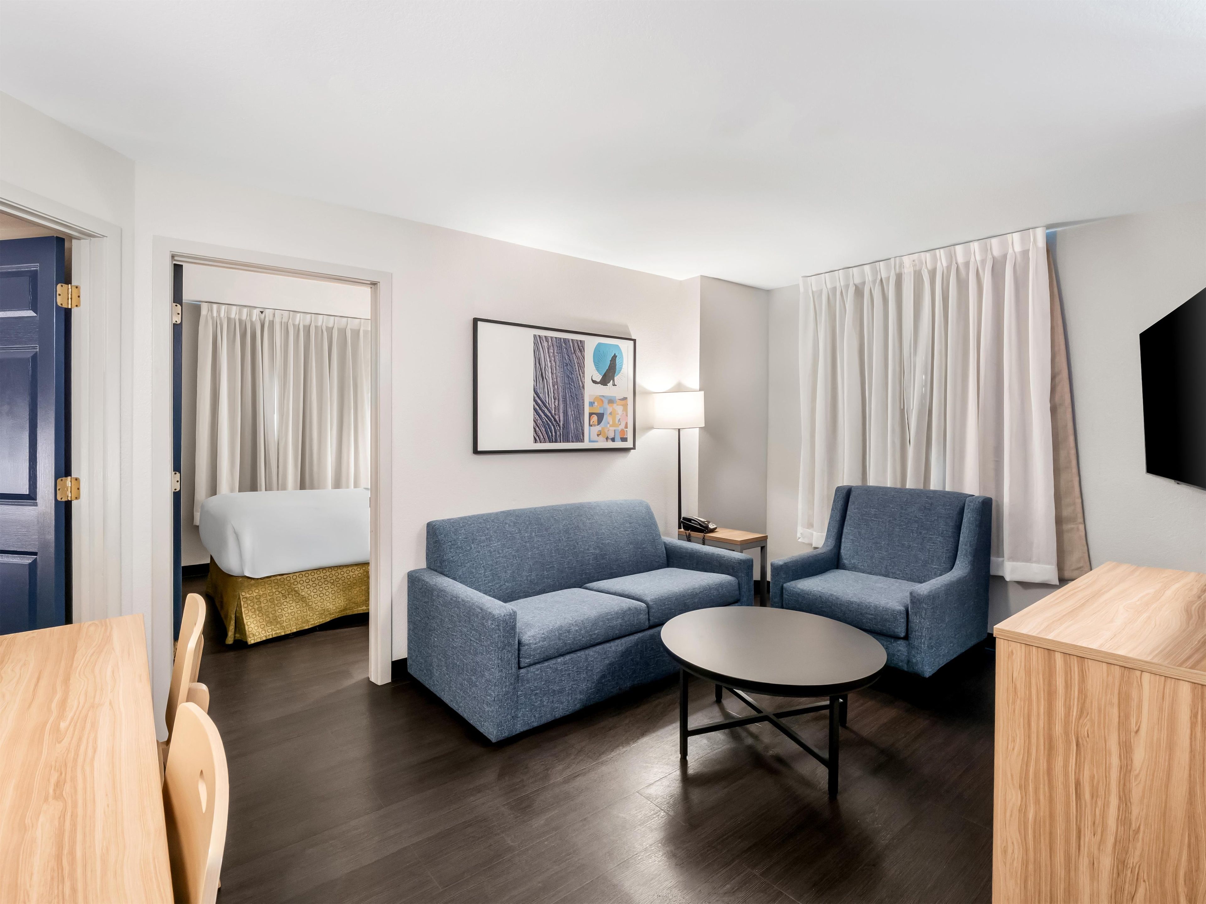 Quarto de hotel com sofá, mesa pequena, luminária e televisão.