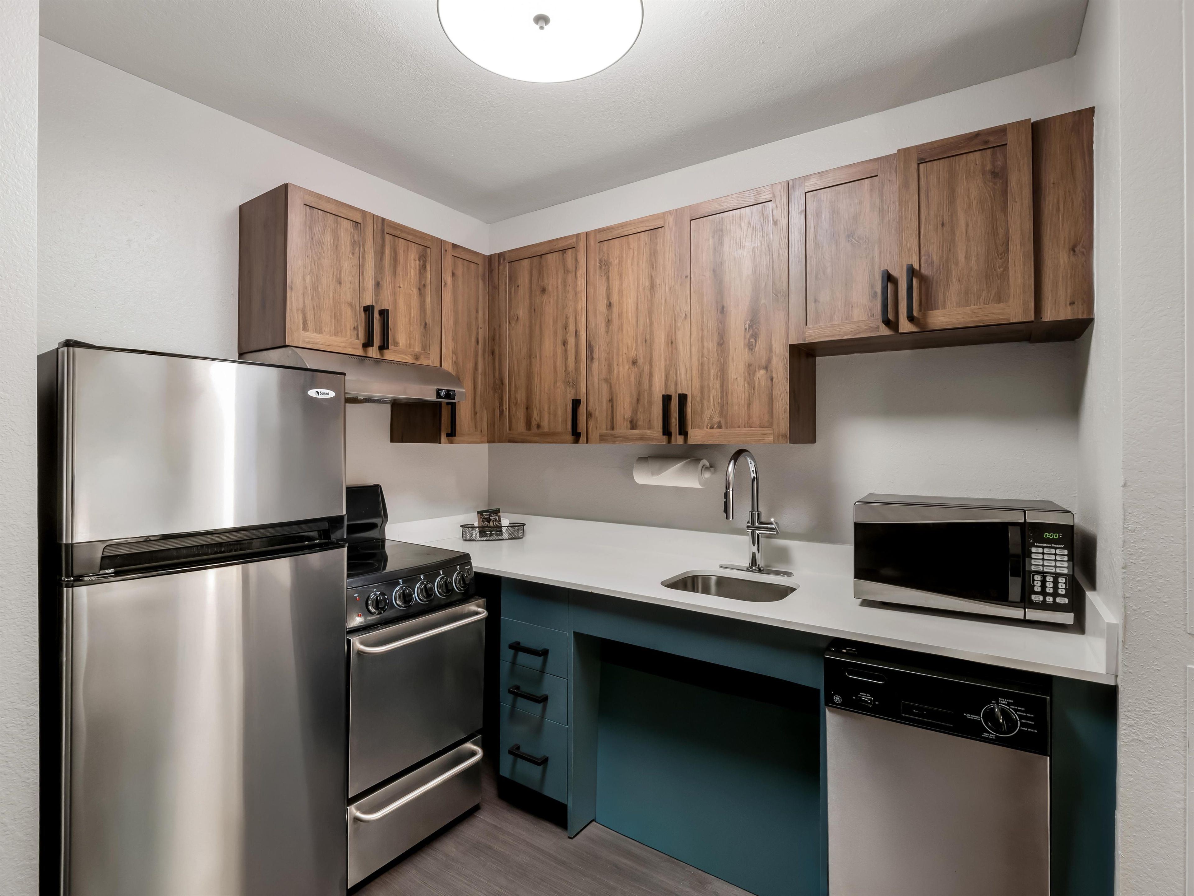 A modern kitchen with stainless steel appliances, wooden cabinets, and a teal backsplash.