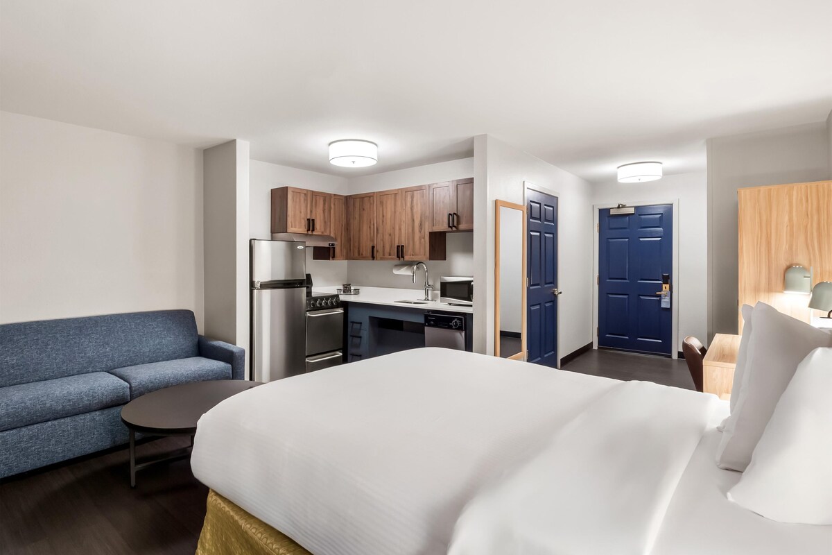 Ein Hotelzimmer mit Bett, einem kleinen Tisch, einer Couch, einer Küchenzeile und einem Badezimmer.