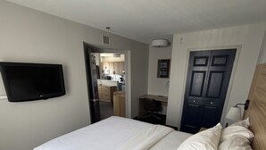Hotellihuone, jossa on sänky, työpöytä, tuoli, seinälle asennettu televisio ja ovi.