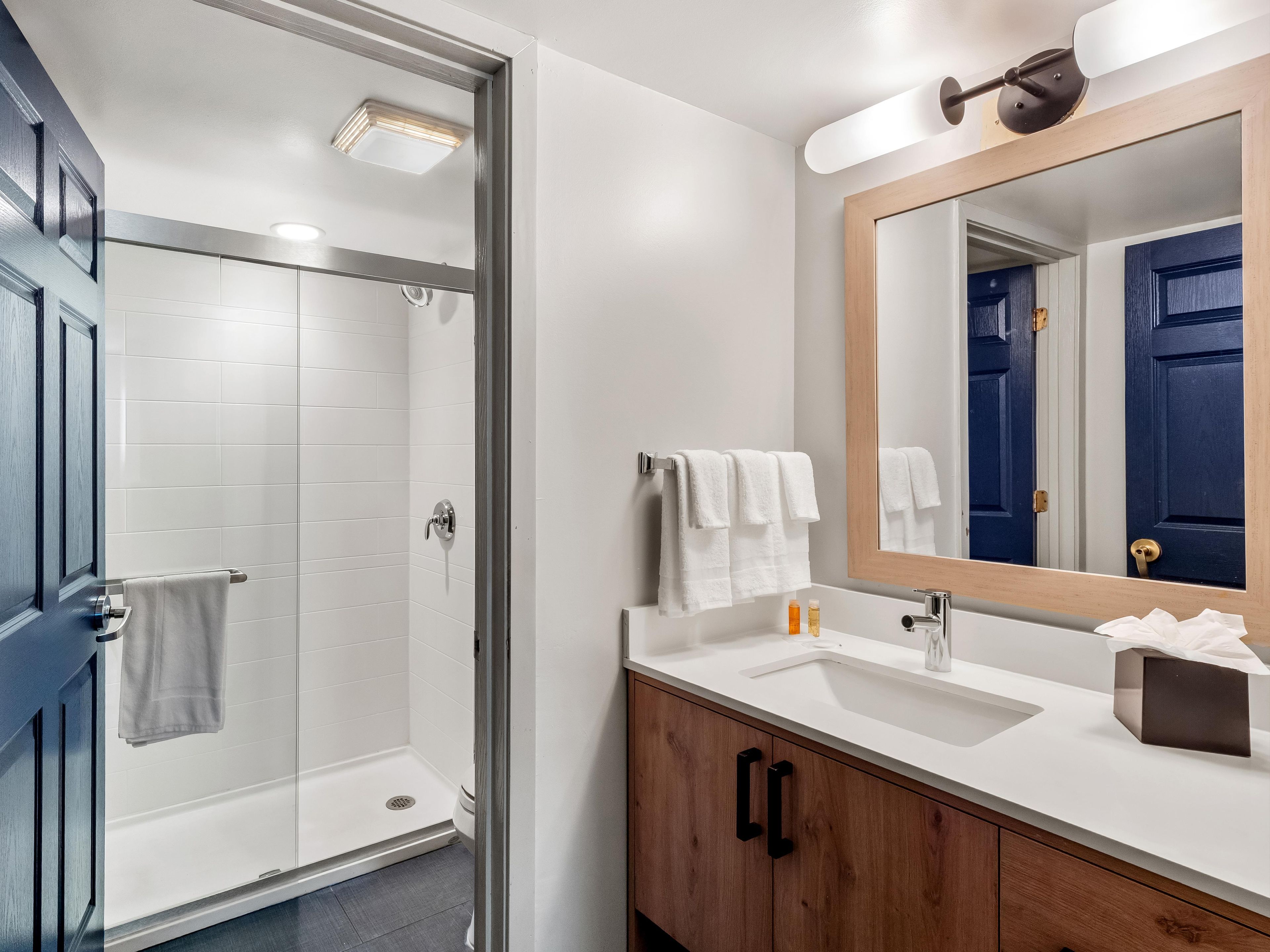 A modern bathroom with a glass shower enclosure, a white sink with a wooden vanity, and a mirror with a wooden frame.