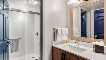 A modern bathroom with a glass shower enclosure, a white sink with a wooden vanity, and a mirror with a wooden frame.