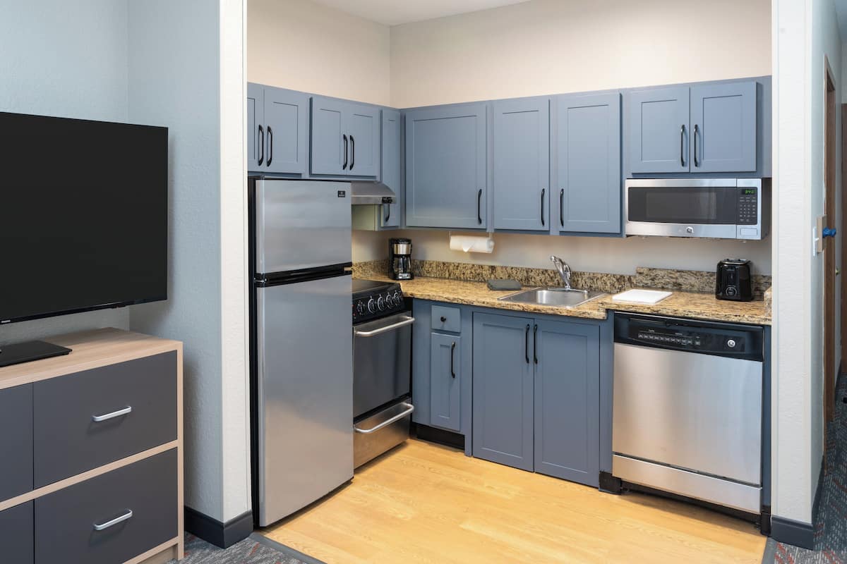 A compact kitchen with grey cabinets, a stainless steel refrigerator, a microwave, a coffee maker, and a dishwasher.