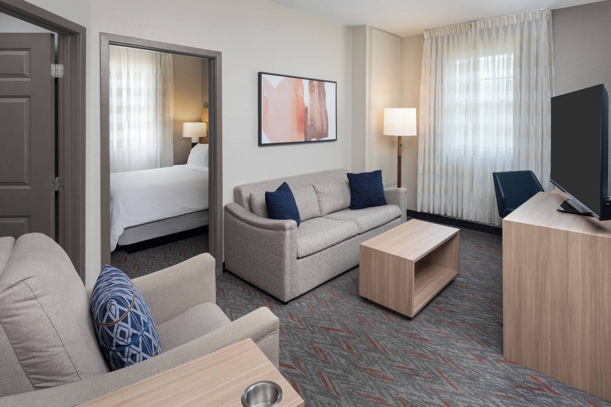 A hotel room with a bed, a sofa, a coffee table, a TV, and a desk.