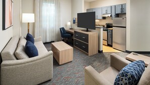 Une chambre d’hôtel équipée d’un canapé, d’un bureau, d’une télévision, d’une kitchenette et d’une table à manger.