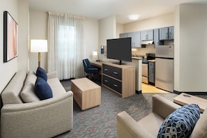 Une chambre d’hôtel équipée d’un canapé, d’un bureau, d’une télévision, d’une kitchenette et d’une table à manger.