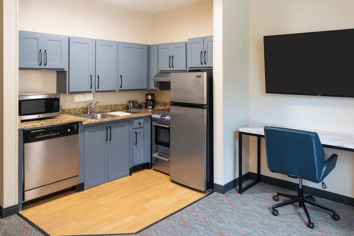 A modern kitchen with grey cabinets, stainless steel appliances, and a built-in oven.