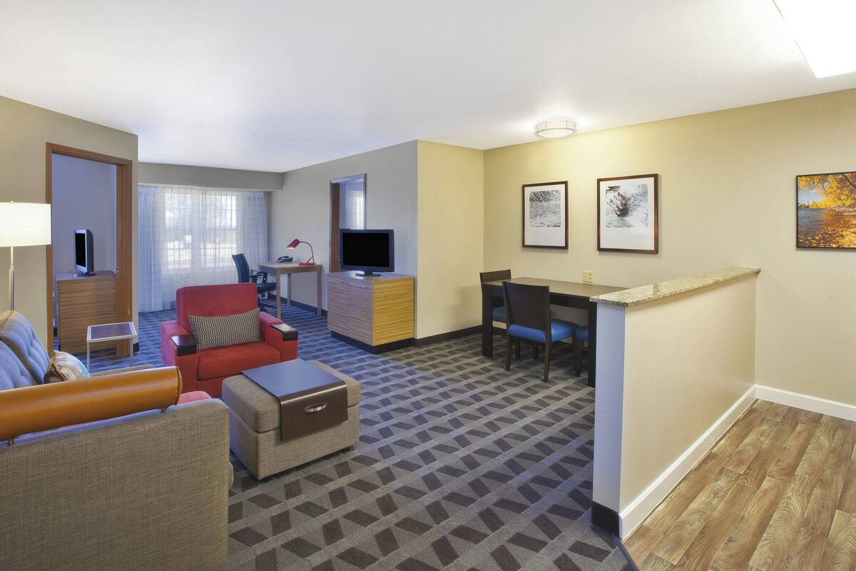 A hotel room with a living area, a dining table, a TV, and artwork on the walls.