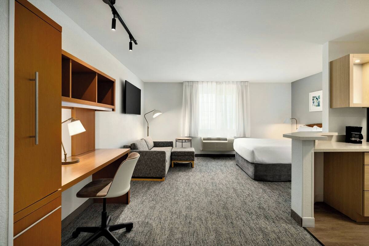 Ein modernes Hotelzimmer mit Schreibtisch, Stuhl, Sofa und Bett.