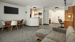 Una habitación de hotel moderna con comedor, kitchenette y sala de estar con sofá y sillones.