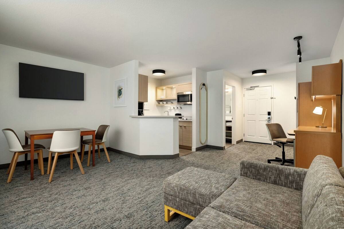 Ein modernes Hotelzimmer mit Essbereich, einer Küchenzeile und einer Sitzecke mit Sofa und Sesseln.