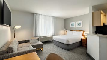 Habitación de hotel con cama, sofá, escritorio, televisión y ventana con cortinas.