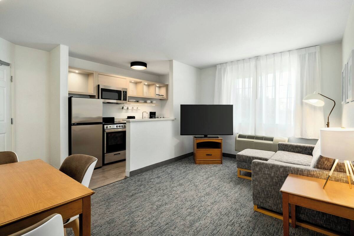 Ein modernes Hotelzimmer mit Küchenzeile, Flachbildfernseher, Sofa und Essbereich.