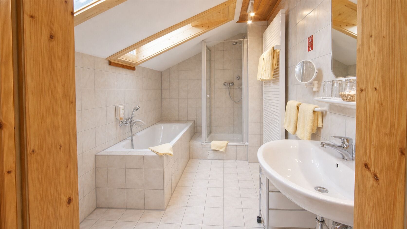 Ein modernes Badezimmer mit Badewanne, Dusche und Waschbecken, Holzbalken an der Decke und Fliesenboden.