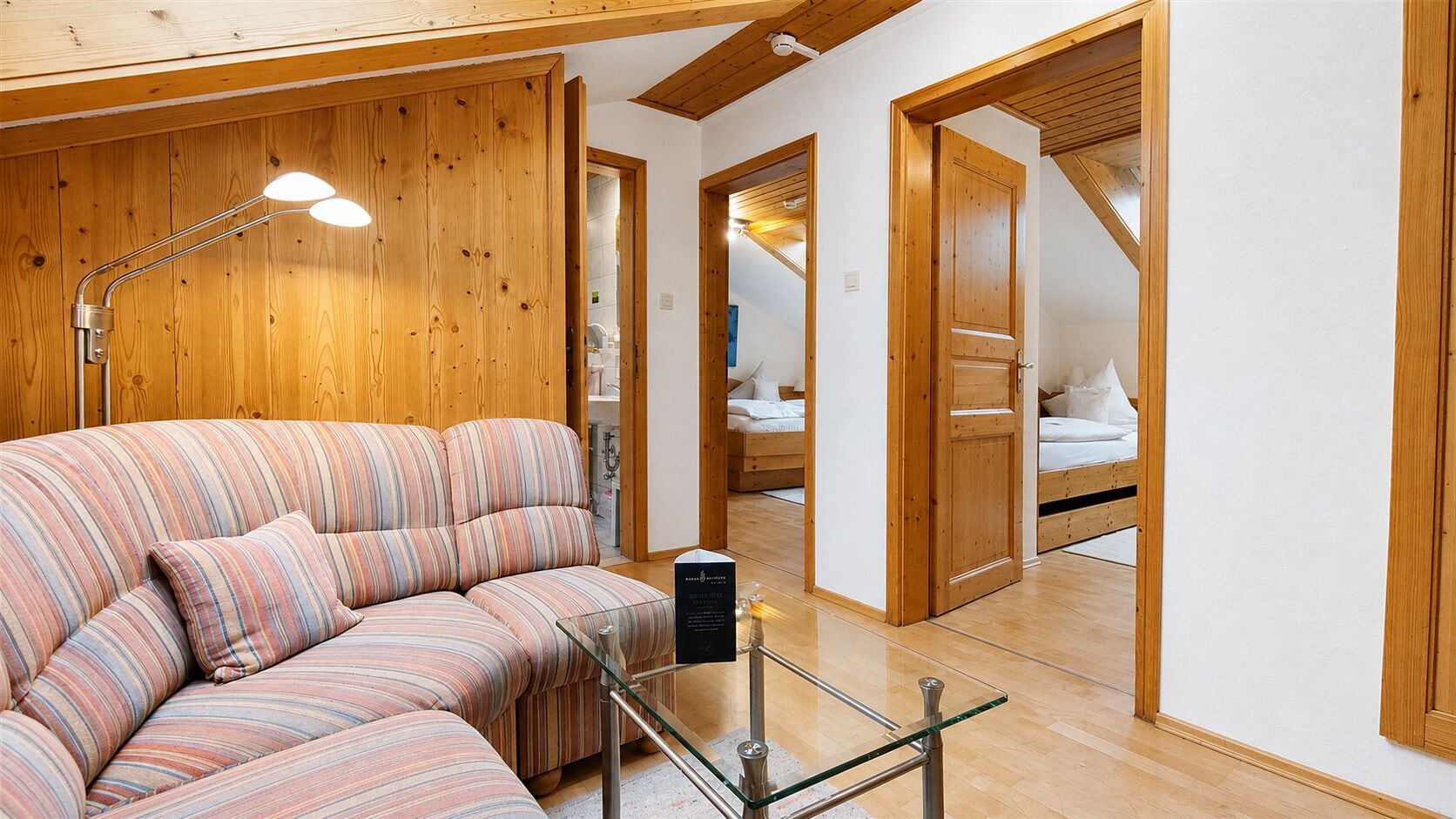 Ein gemütliches Zimmer mit einem gestreiften Sofa, einem Glastisch und Holzwänden.
