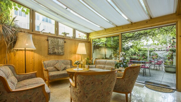 A sunlit room with wooden walls, a large window, and a view of a garden. - Hotel Brunner (Amberg)