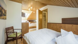 A bedroom with a wooden ceiling, a bed with white bedding, a wooden chair, and a painting on the wall. - Hotel Brunner (Amberg)