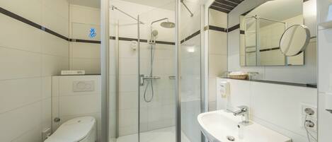 A modern bathroom with a glass-enclosed shower, a white toilet, and a sink with a mirror.