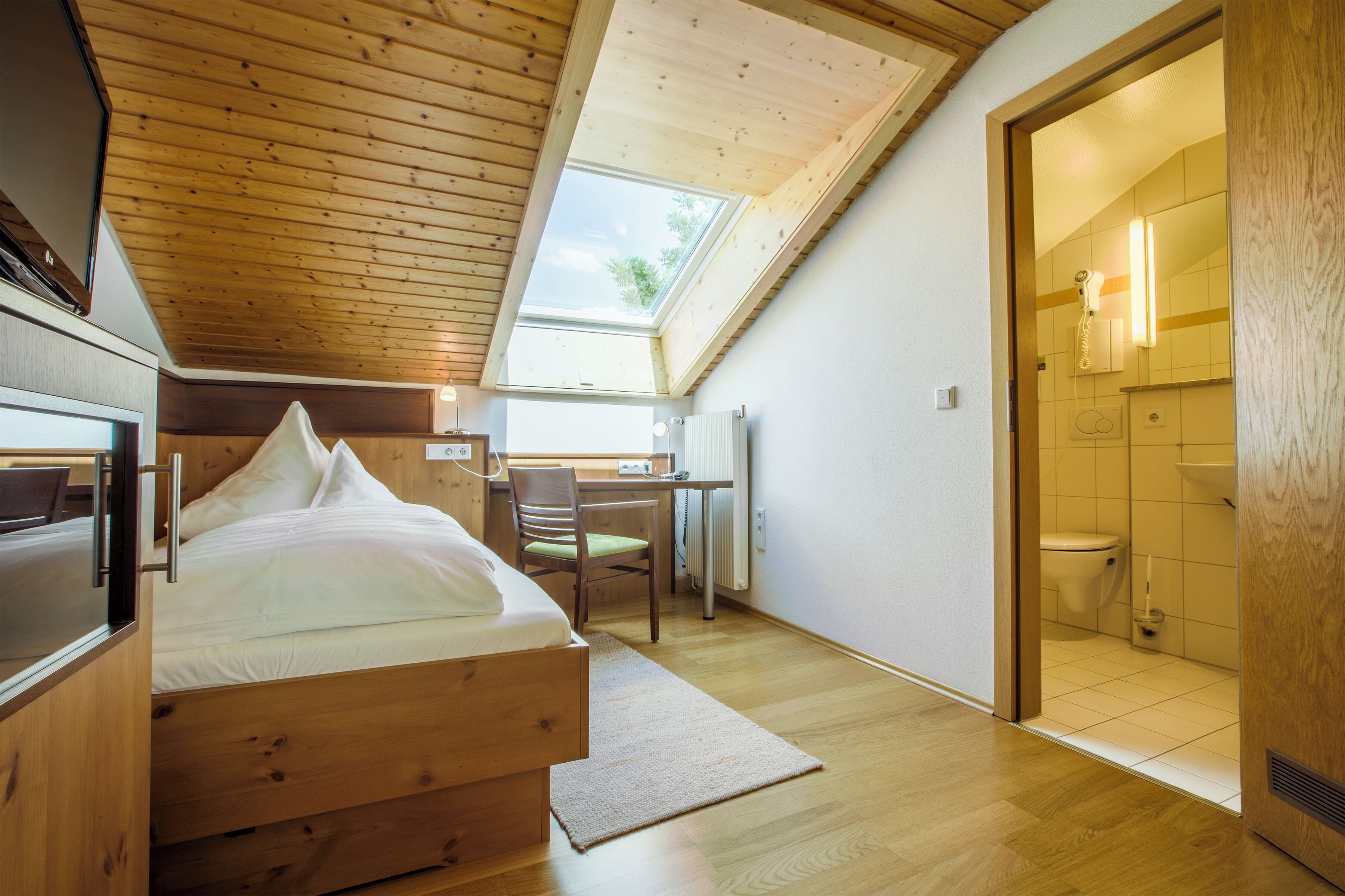 A bedroom with a wooden bed, a desk, and a skylight.