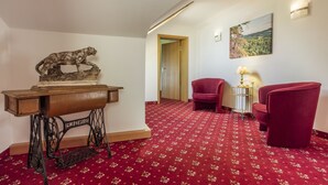 A room with a red carpet, a wooden desk with a lion sculpture, two red chairs, and a painting on the wall. - Hotel Brunner (Amberg)