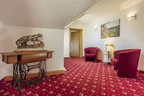Ein Zimmer mit rotem Teppich, einem Holztisch mit einer Löwenskulptur, zwei roten Stühlen und einem Gemälde an der Wand.
