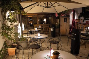 An outdoor seating area with round tables and chairs, a large umbrella providing shade, and potted plants. - Hotel Brunner (Amberg)