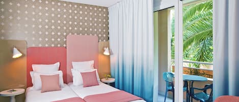 Habitación de hotel con una cama grande, dos mesitas de noche, una mesita redonda pequeña y un balcón con sillas.