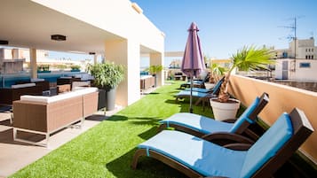 A rooftop terrace with lounge chairs, a bar area, and potted plants.