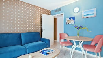Ein Zimmer mit einem blauen Sofa, einem runden Holztisch mit zwei roten Stühlen, einer kleinen Vase mit Blumen und einer Wand mit blau-weißem Muster.