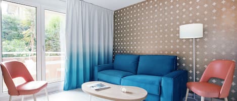 Una sala moderna con un sofá azul, dos sillas rojas, una mesa de centro de madera y una pared con diseño.