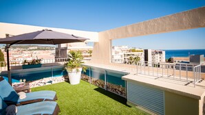Une terrasse sur le toit avec une piscine, des chaises longues et une vue sur la mer.