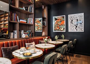 A cozy cafe with leather seating, bookshelves, and artwork on the walls.