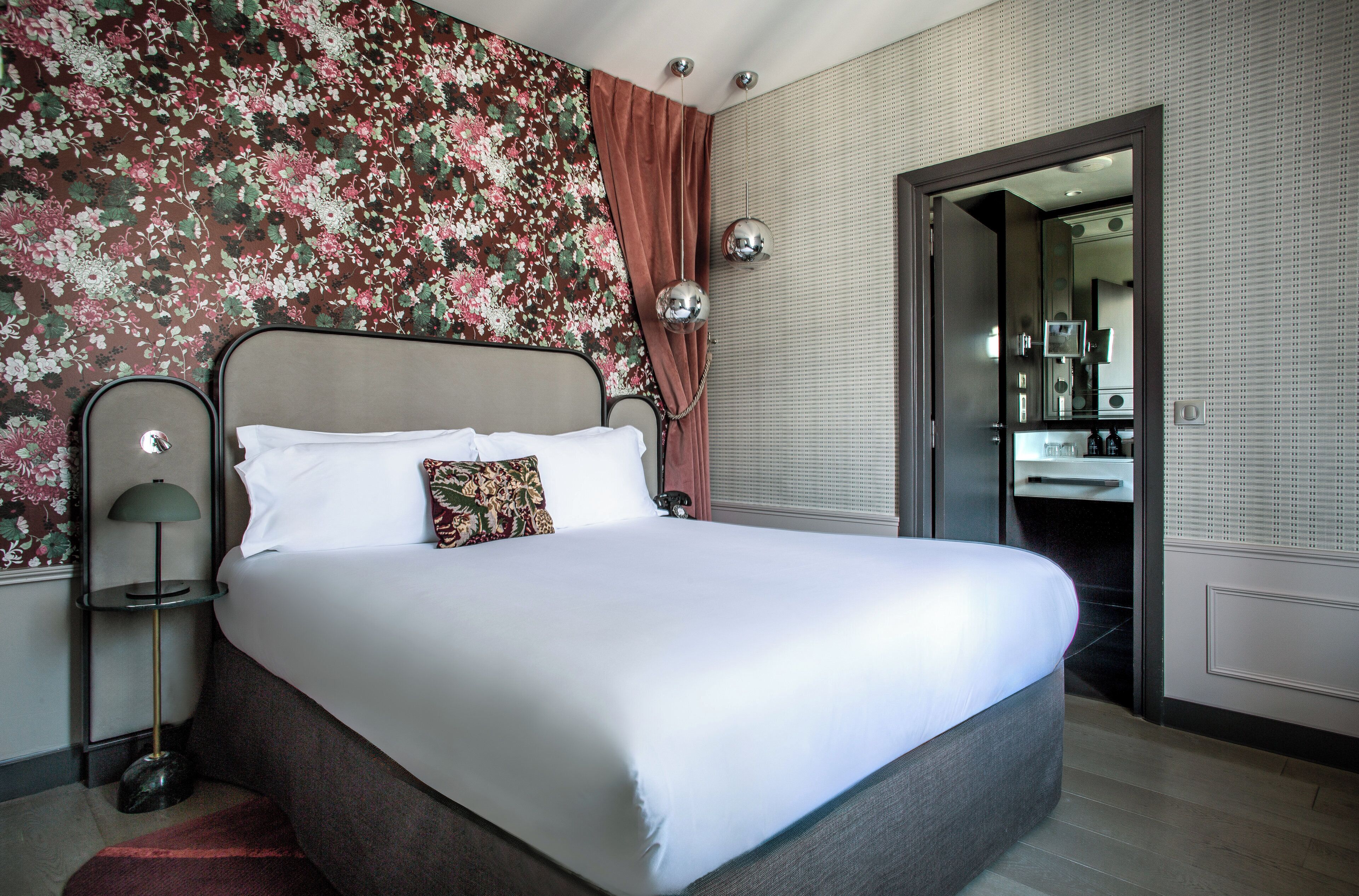 Una cama bien tendida con sábanas blancas, un cojín estampado con motivos florales y un cabecero moderno.