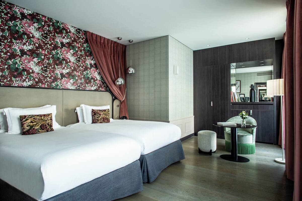 A hotel room with a large bed, a small table, a chair, a mirror, and a decorative wall.