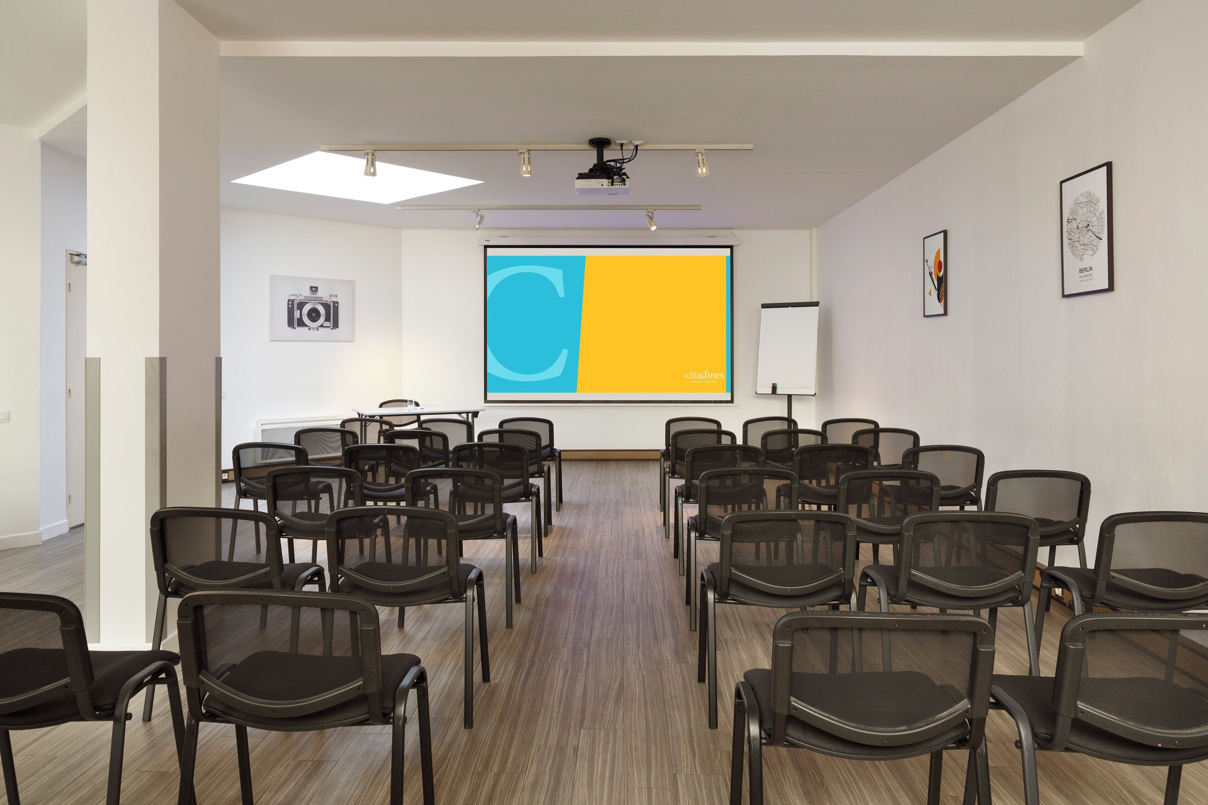 Un salón de conferencias con filas de sillas, una pantalla de proyector y una pizarra.