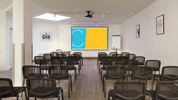 Un salón de conferencias con filas de sillas, una pantalla de proyector y una pizarra.