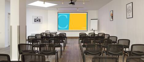 Un salón de conferencias con filas de sillas, una pantalla de proyector y una pizarra.