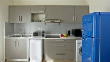 A modern kitchen with grey cabinets, a blue refrigerator, a dishwasher, a toaster, and a kettle.
